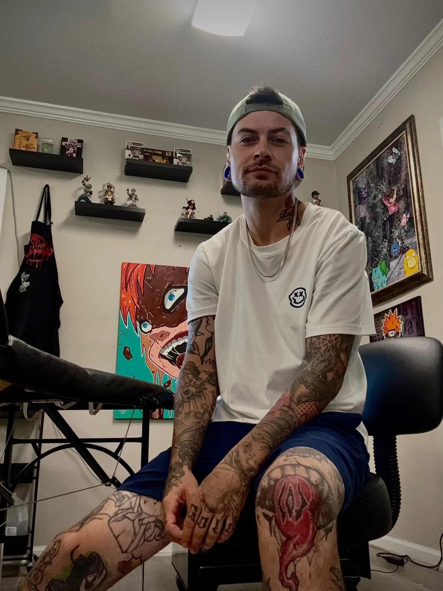 Cory Veron, seated, in a white T-shirt with tattooed arms and legs
